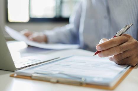 Foto: Person mit Dokumenten und Laptop